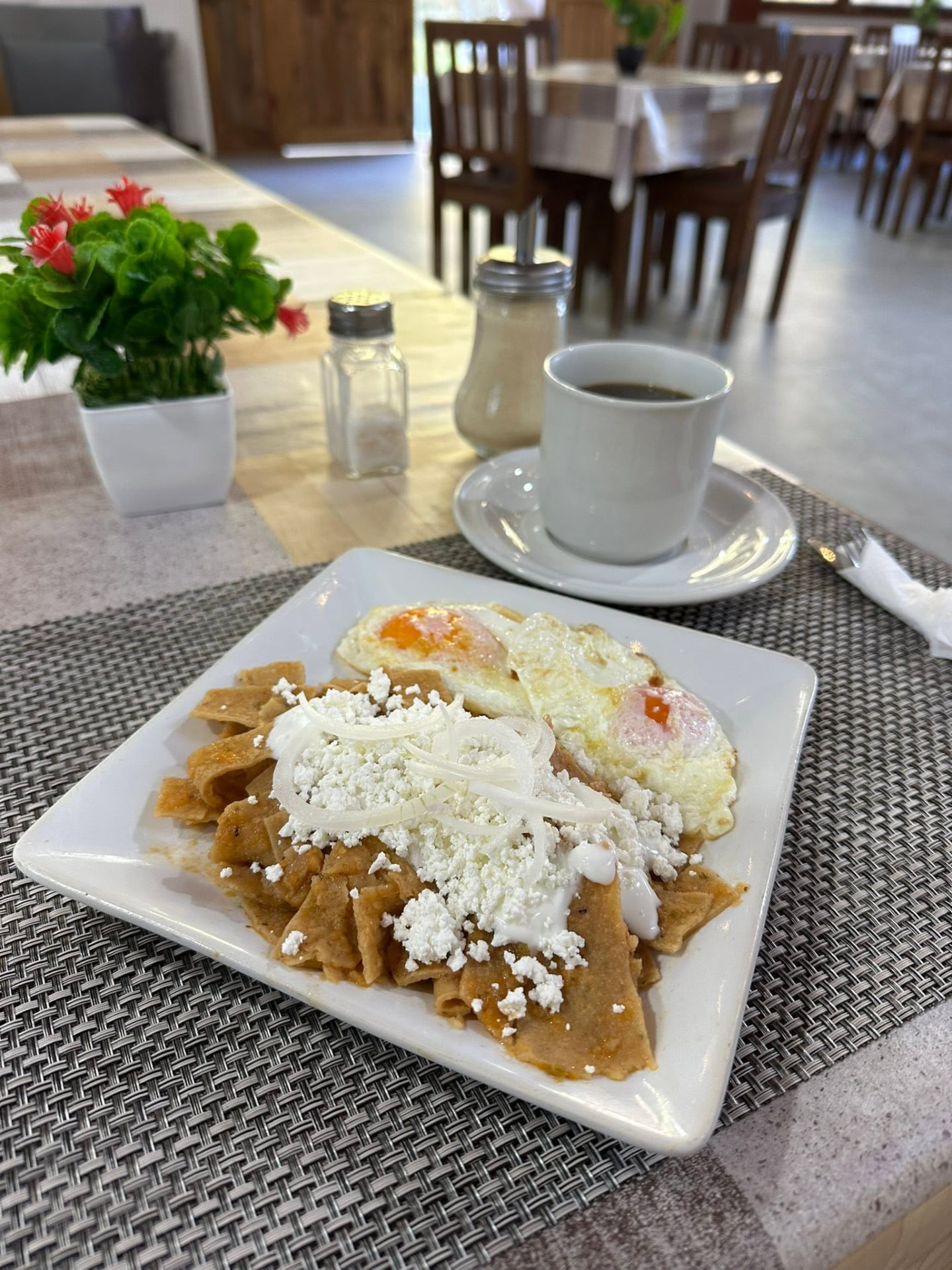 Chilaquiles rojos con huevo estrellado, queso y crema, acompañados de café
