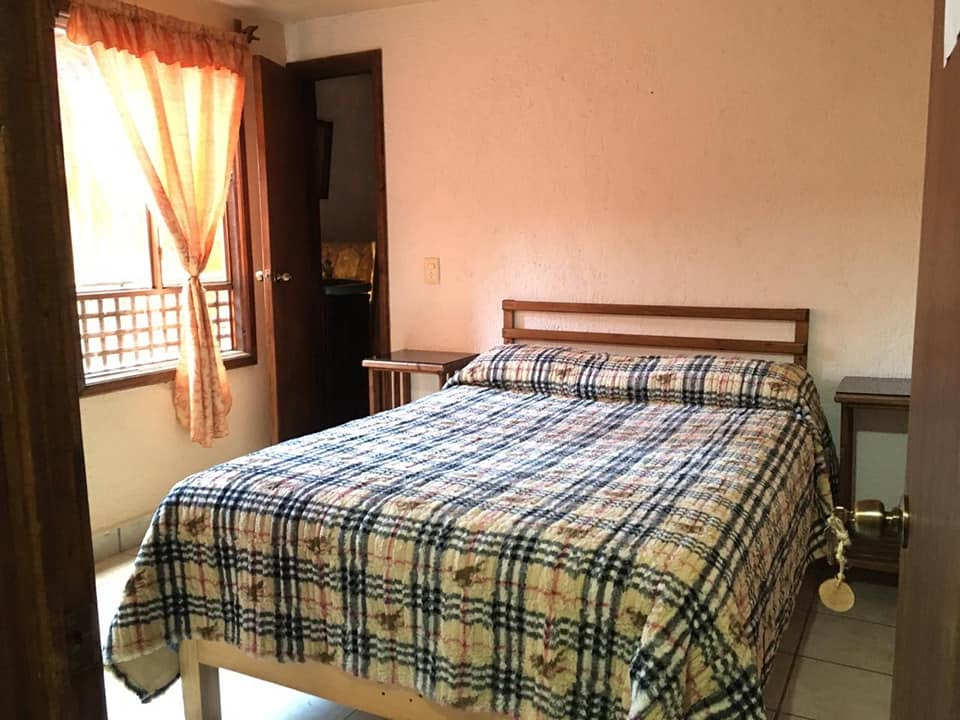 Habitación matrimonial con cama tendida, cortina cálida y baño propio
