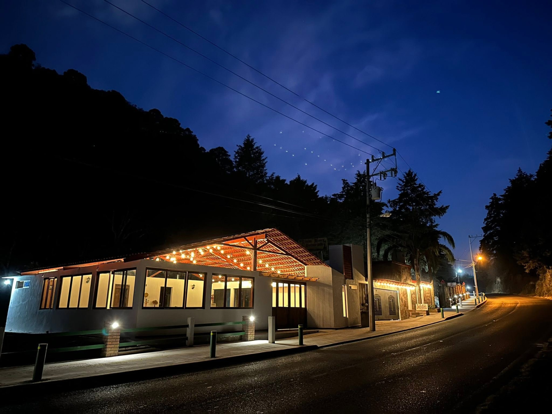 Fachada del restaurante iluminada al anochecer, vista desde la carretera